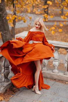 Stylish woman in an orange dress poses amid autumnal leaves in Istanbul for fashion photography.