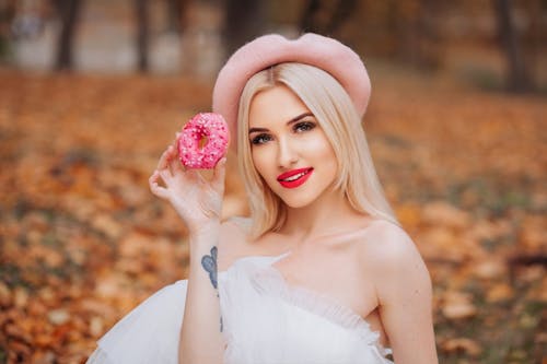 Blonde Woman in White Tulle Dress and Pink Beret Holding a Donut