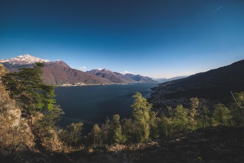 Free A breathtaking view of an alpine lake surrounded by mountains and lush forests under a clear blue sky. Stock Photo