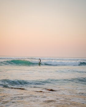 A lone surfer enjoying the rolling waves at sunrise on Bali's scenic seashore.