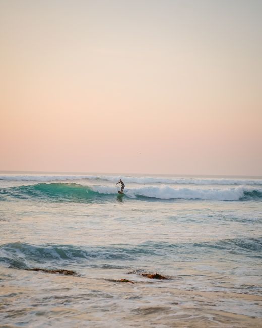 A lone surfer enjoying the rolling waves at sunrise on Bali's scenic seashore.