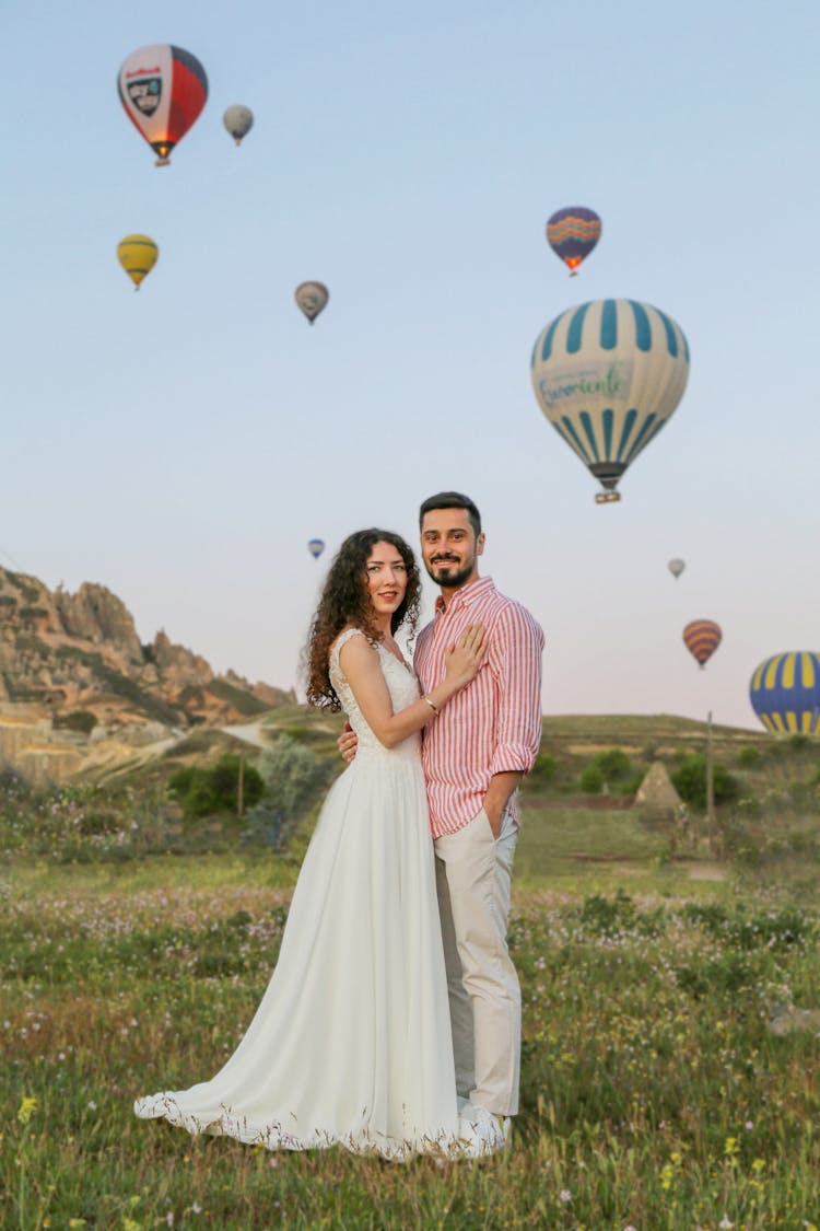 Embracing Couple In A Glade With Hot Air Balloons Floating In The Background