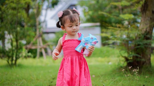 Little Girl in Pink Dress Playing with Toy in Yard