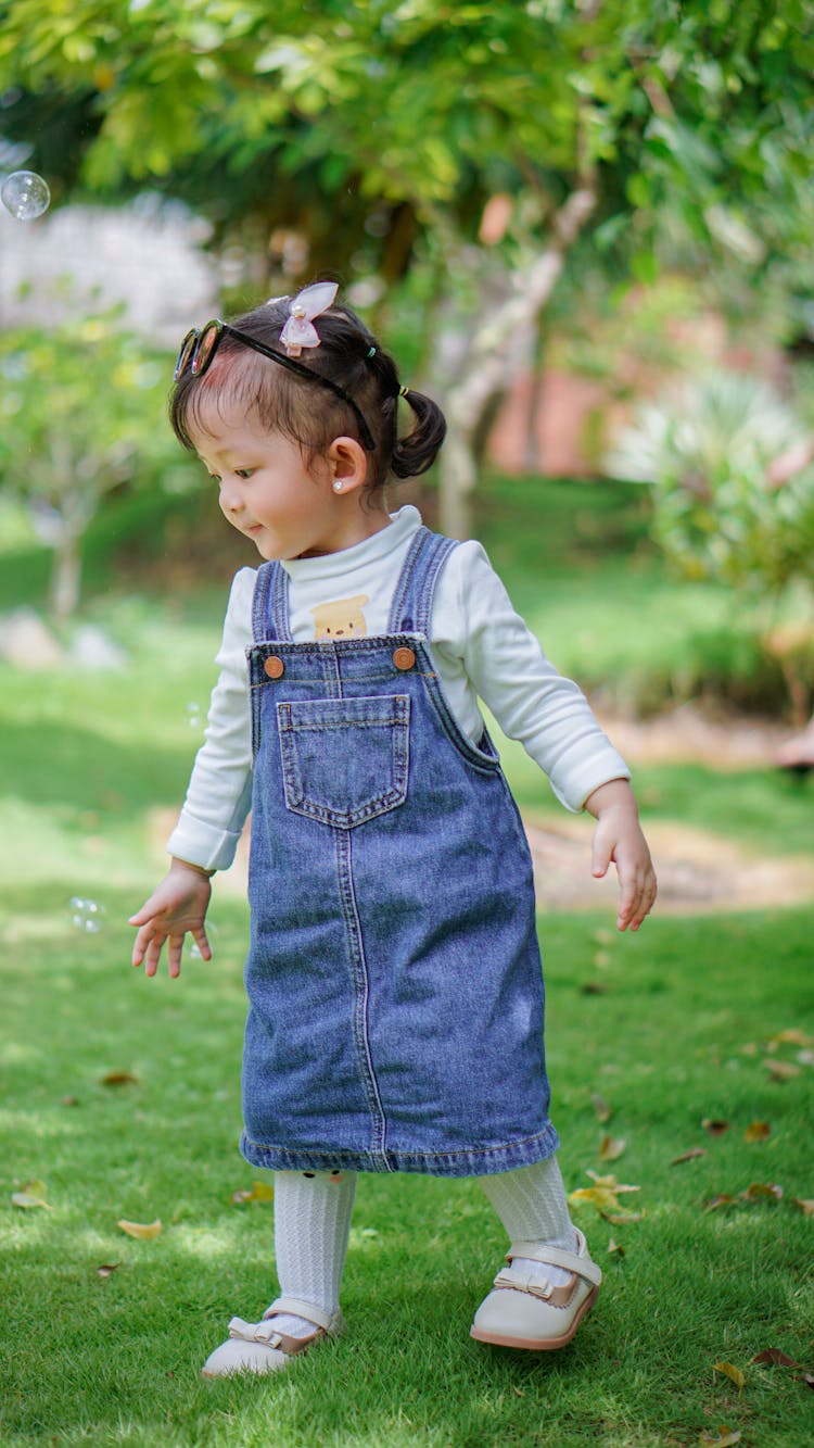 Little Girl In Denim Dress Walking On Grass