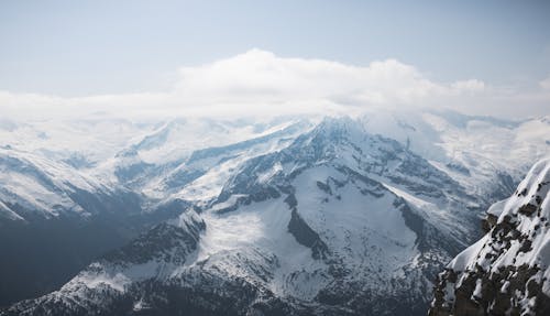 A person standing on top of a mountain looking at the snow covered mountains