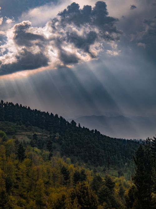 Free Breathtaking view of sun rays breaking through clouds over a lush mountain forest, capturing nature's serene beauty during sunset. Stock Photo