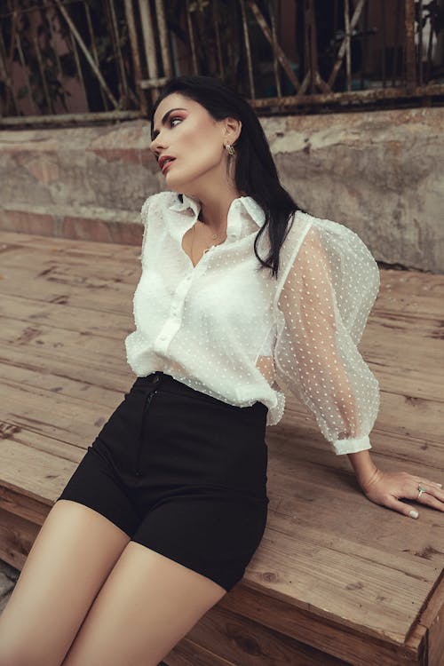 Female Model Wearing a White Shirt and a Black Mini Skirt Leaning on a Wooden Surface