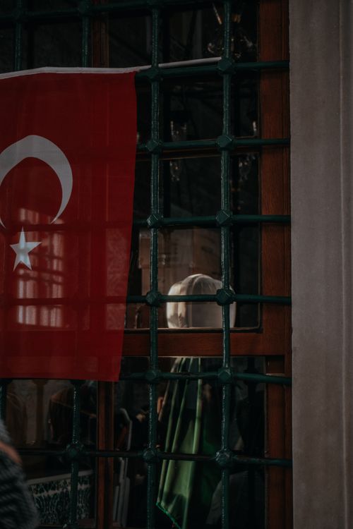 Free A nostalgic image of a Turkish flag hanging over an old-fashioned window with a courtyard view. Stock Photo