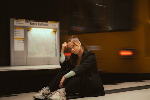 Young Woman Sitting on a Subway Station Platform with a Moving Train in the Background 