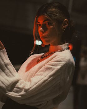 Young woman in Berlin with red light casting a moody night scene, wearing a white sweater.