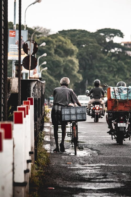 Elderly Man Walking with Bicycle on Road