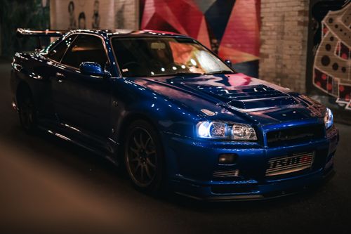 Free A striking blue sports car parked in a vibrant urban mural street at night. Stock Photo
