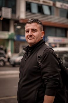 Middle-aged man in black jacket standing on city street, portraying urban fashion and lifestyle.