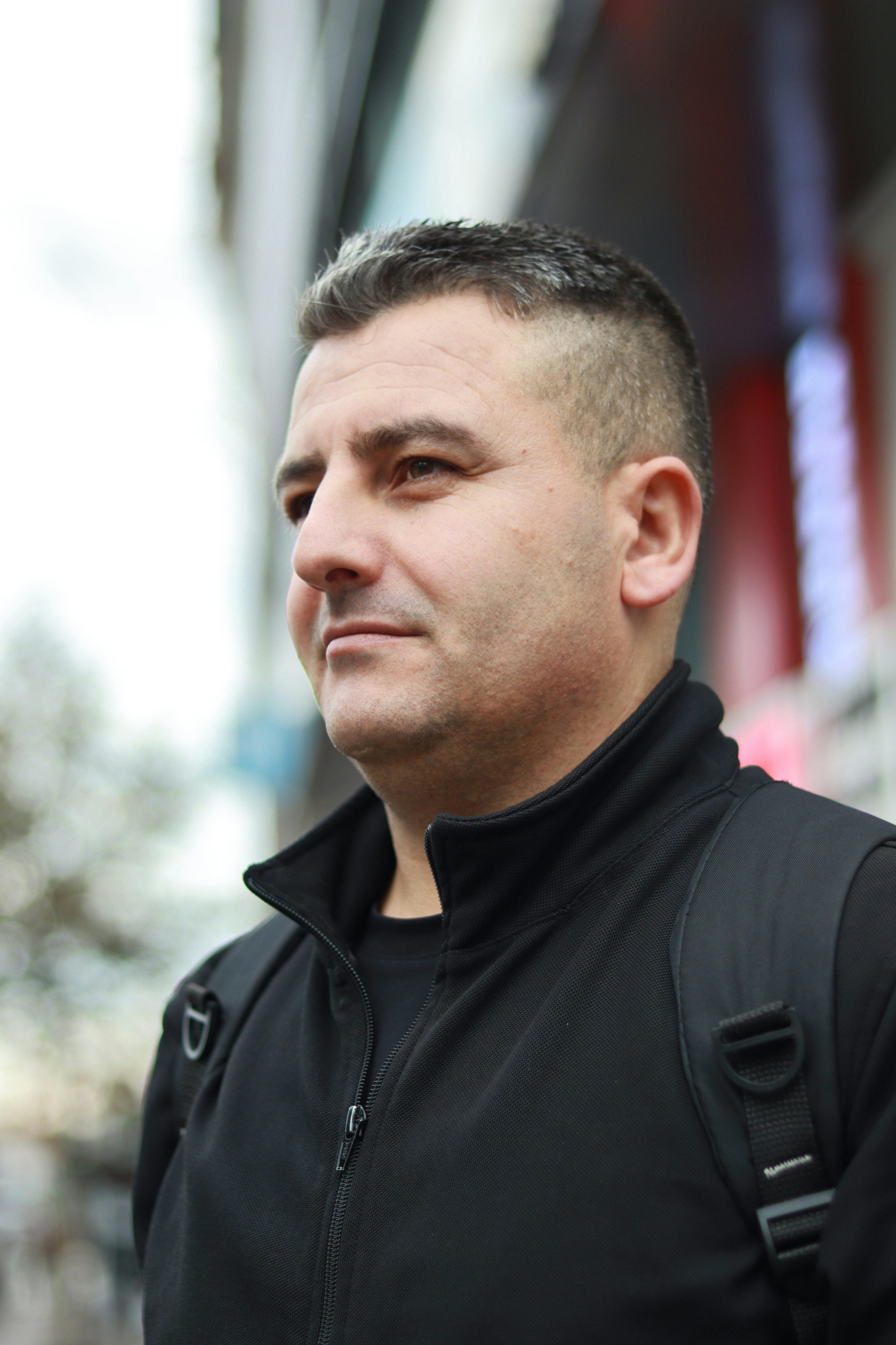 Portrait of a man in a black jacket and backpack. Captured outdoors with blurred background.