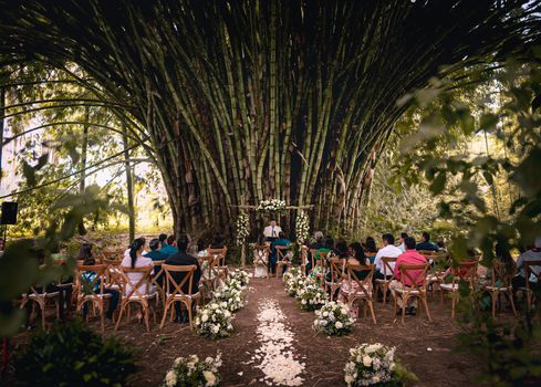 Beautiful outdoor wedding ceremony in a lush forest setting with elegant floral decorations and seated guests.