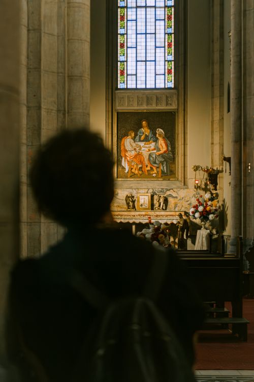 Free Silhouetted figure observing a church altar with religious art and stained glass window. Stock Photo