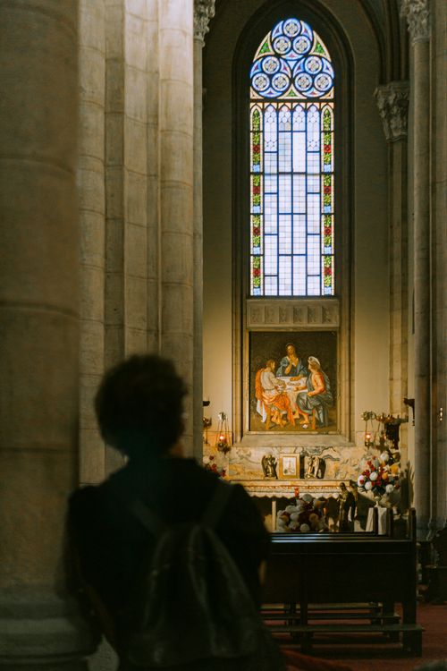 Free A man silhouetted inside a cathedral looking towards a stained glass window and ornate altar. Stock Photo