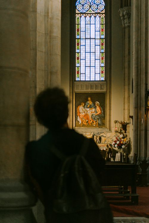 Free A person stands in silhouette looking at a beautifully lit church altar with stained glass windows. Stock Photo
