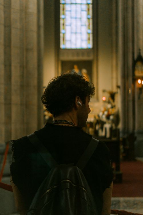 Free A man standing in a church, viewed from behind, wearing headphones and backpack. Stock Photo