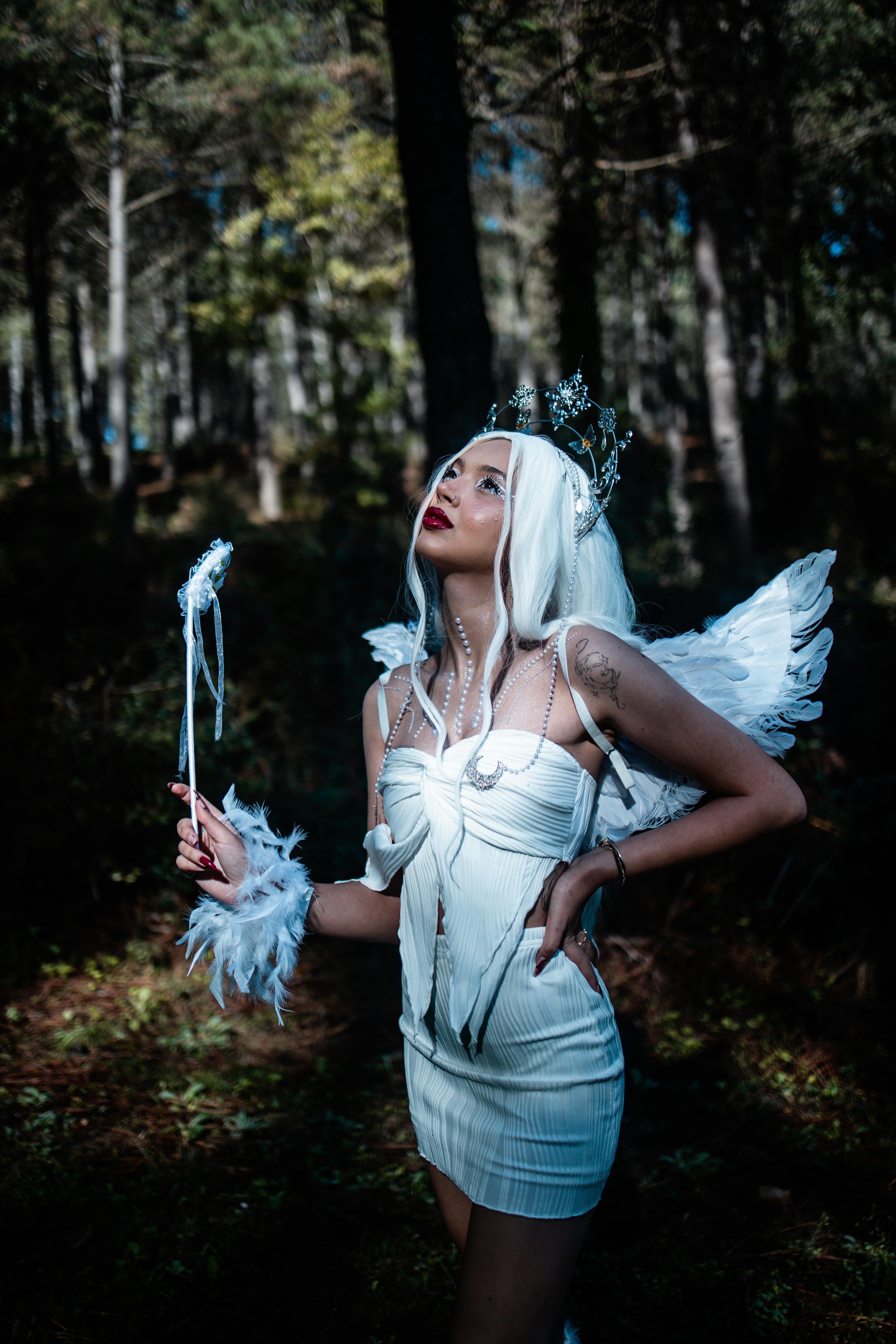 A woman dressed as a fairy with wings and wand in a mystical forest setting.