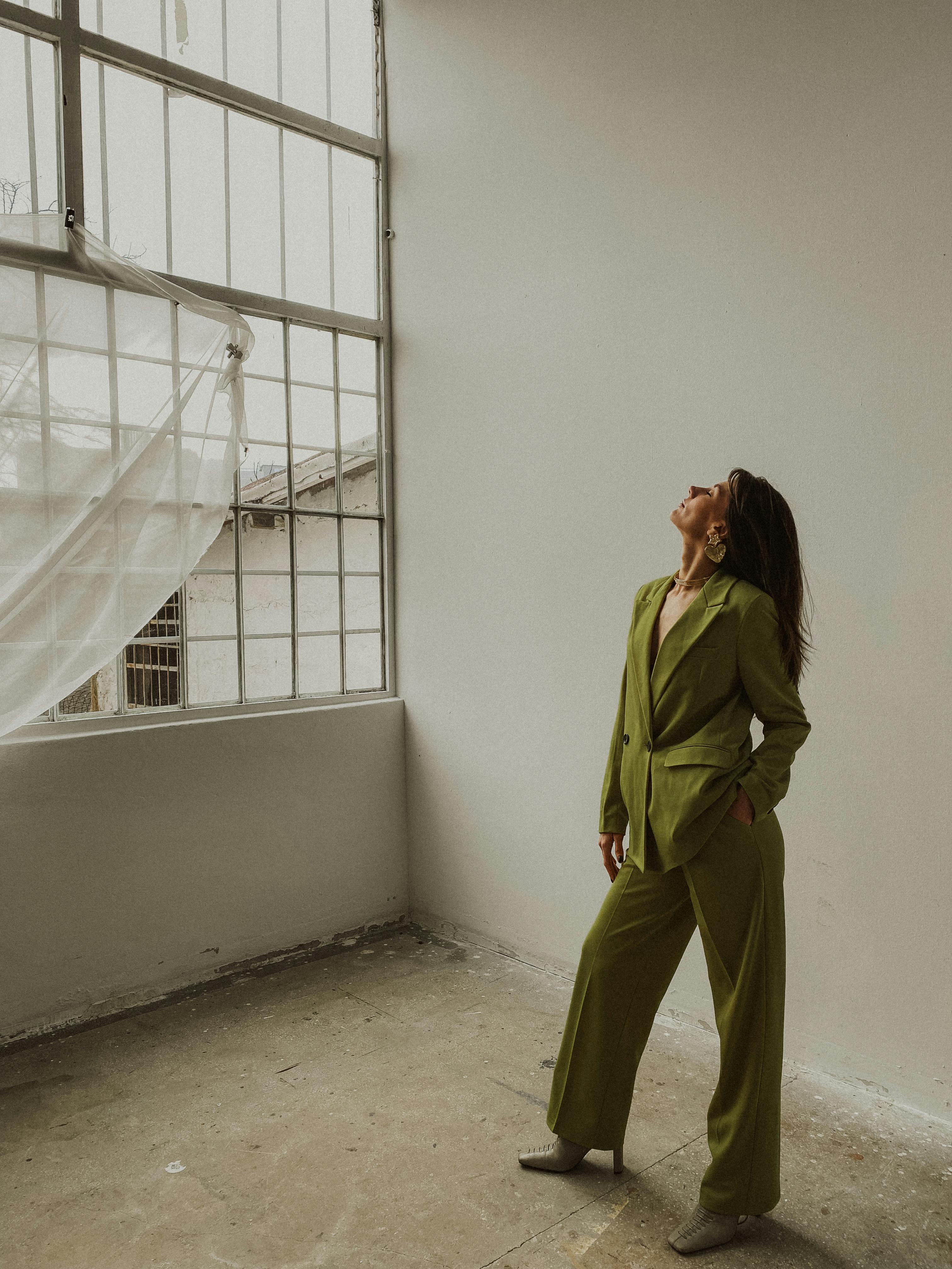 Elegant woman in a green suit posing with confidence in an industrial-style room.