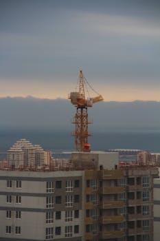 Aerial view of a construction crane above a city building at sunset, showcasing urban skyline.