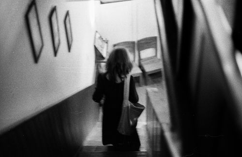 Free Candid black and white photo of a woman descending indoor stairs with framed artwork on the wall. Stock Photo