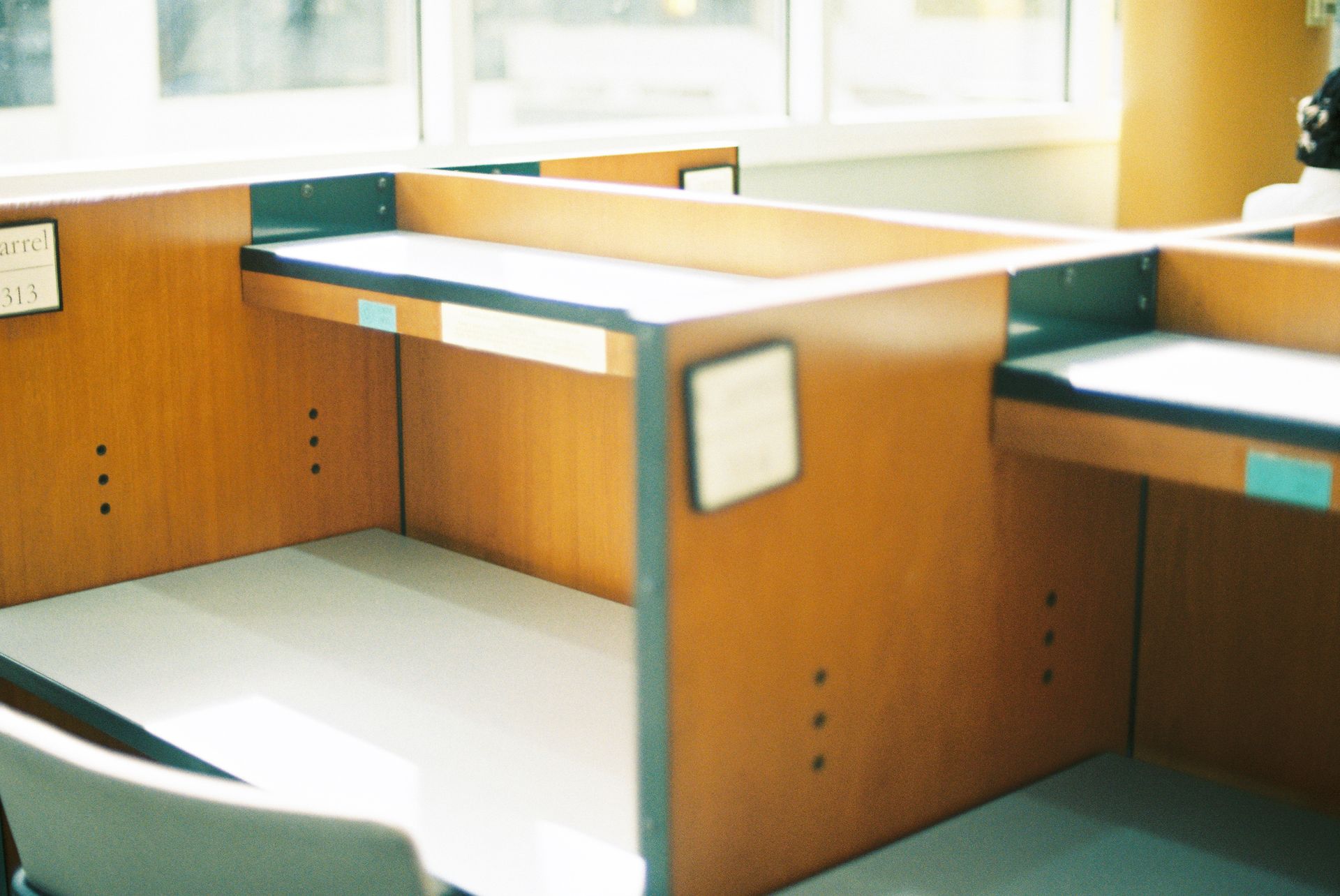 Empty wooden cubicles in a sunlit office space, offering a modern professional ambience.