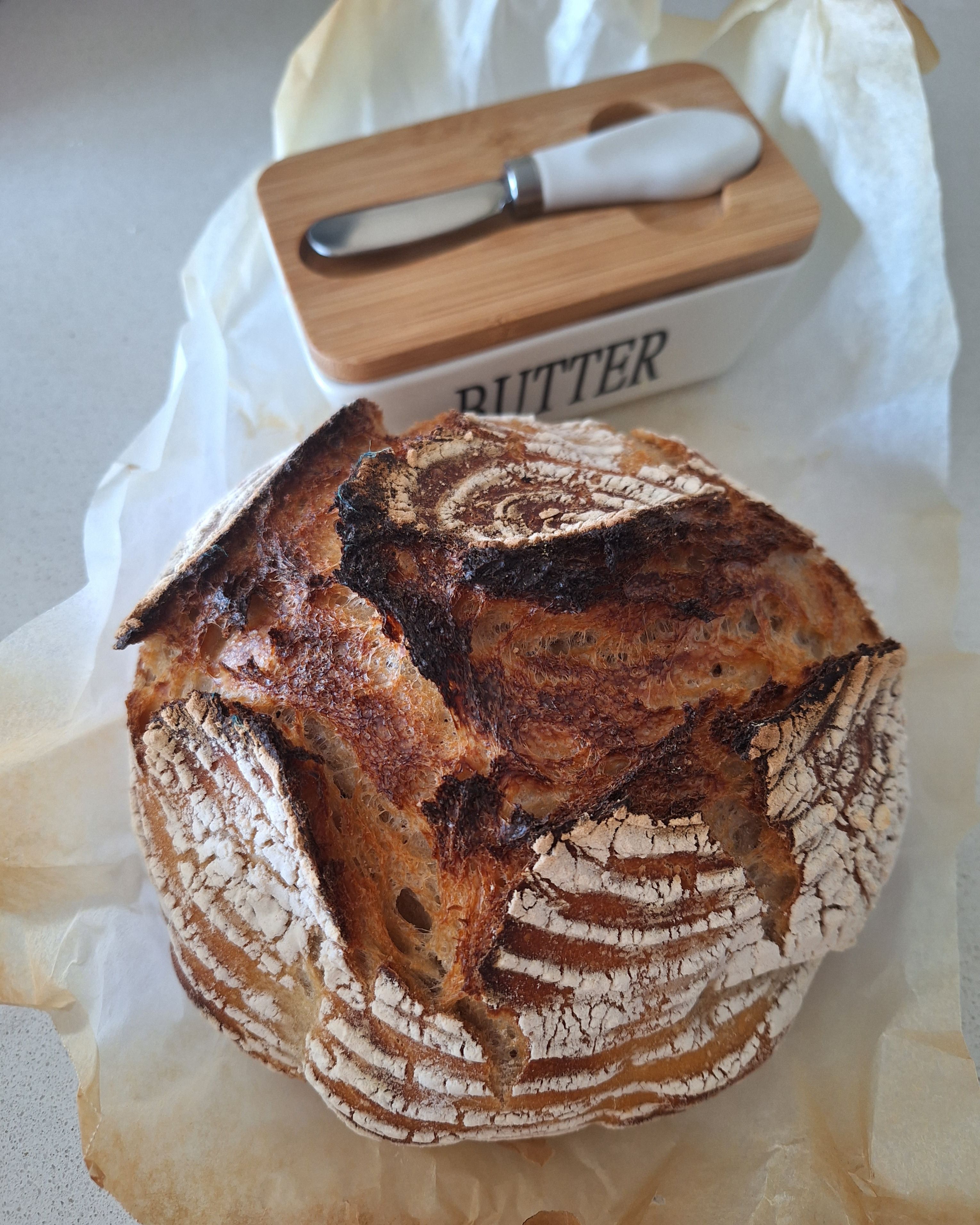 Rustic homemade sourdough bread with butter dish in kitchen setting.