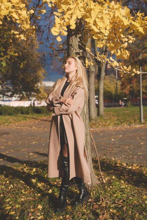 Free Elegant woman in coat standing amidst autumn foliage with closed eyes. Stock Photo