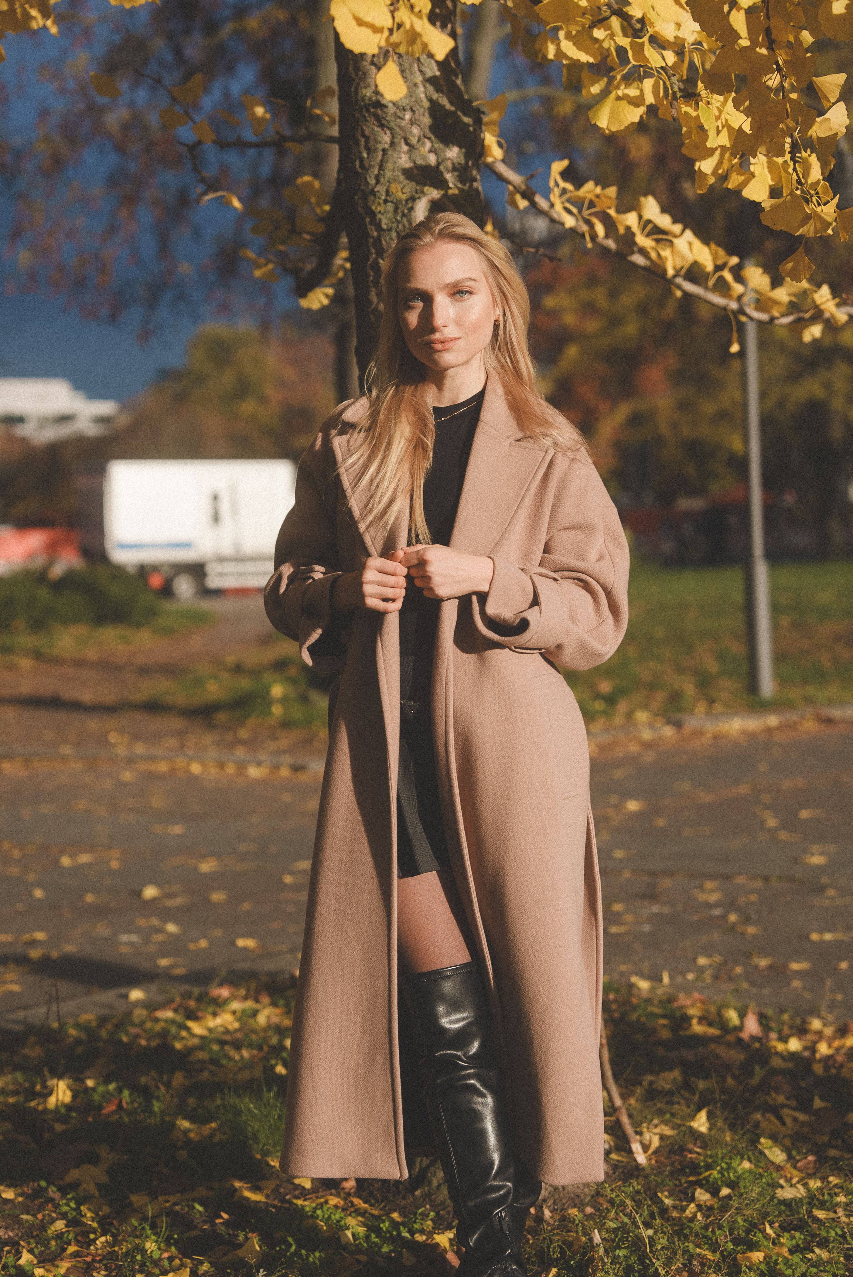 Woman in an oversized camel wool coat and black knee-high boots in an autumn park — camel and tall boots equestrian fall outfit