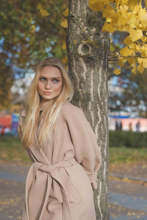 Free Blonde woman in a beige coat enjoying a sunny autumn day in a park. Stock Photo