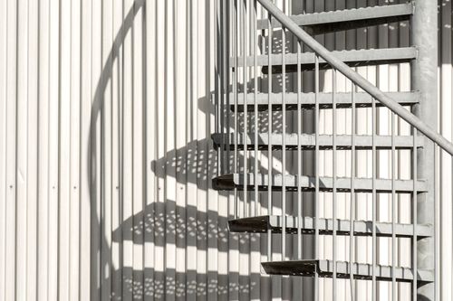 Free Geometric shadows from a steel spiral staircase on a corrugated wall, urban architectural detail. Stock Photo