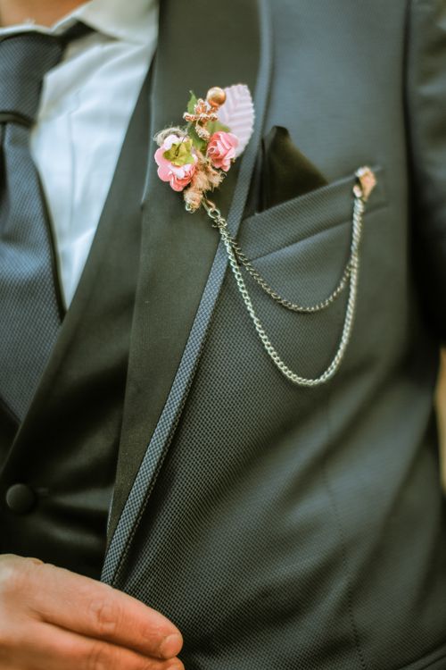 Free Close-up of a groom's suit featuring a stylish floral boutonniere and chain accessory. Stock Photo