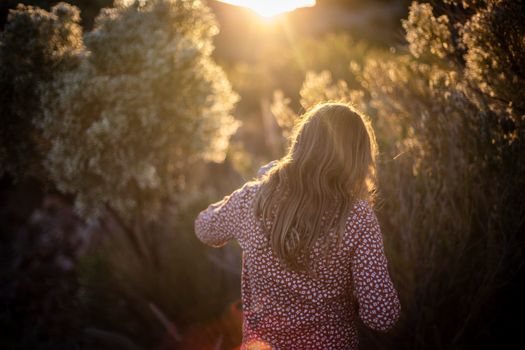 A woman with blonde hair walks through a sunlit field at sunset, capturing tranquility.