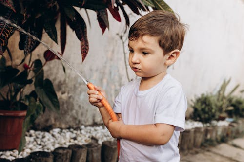 Free Little Boy with Hose Splashing Water in Yard Stock Photo