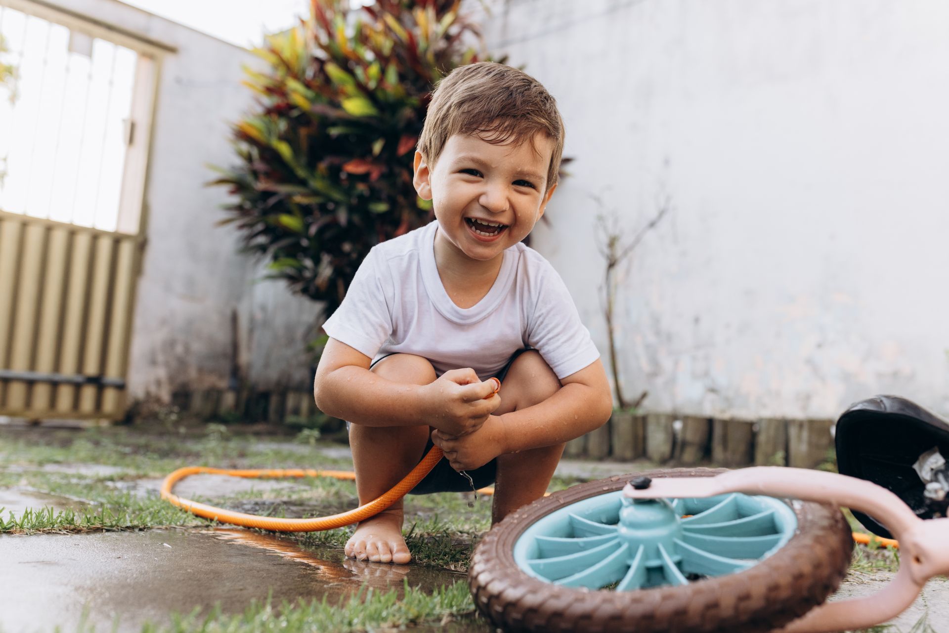 Smiling Boy Squatting with Garden Hose by Bike Wheel