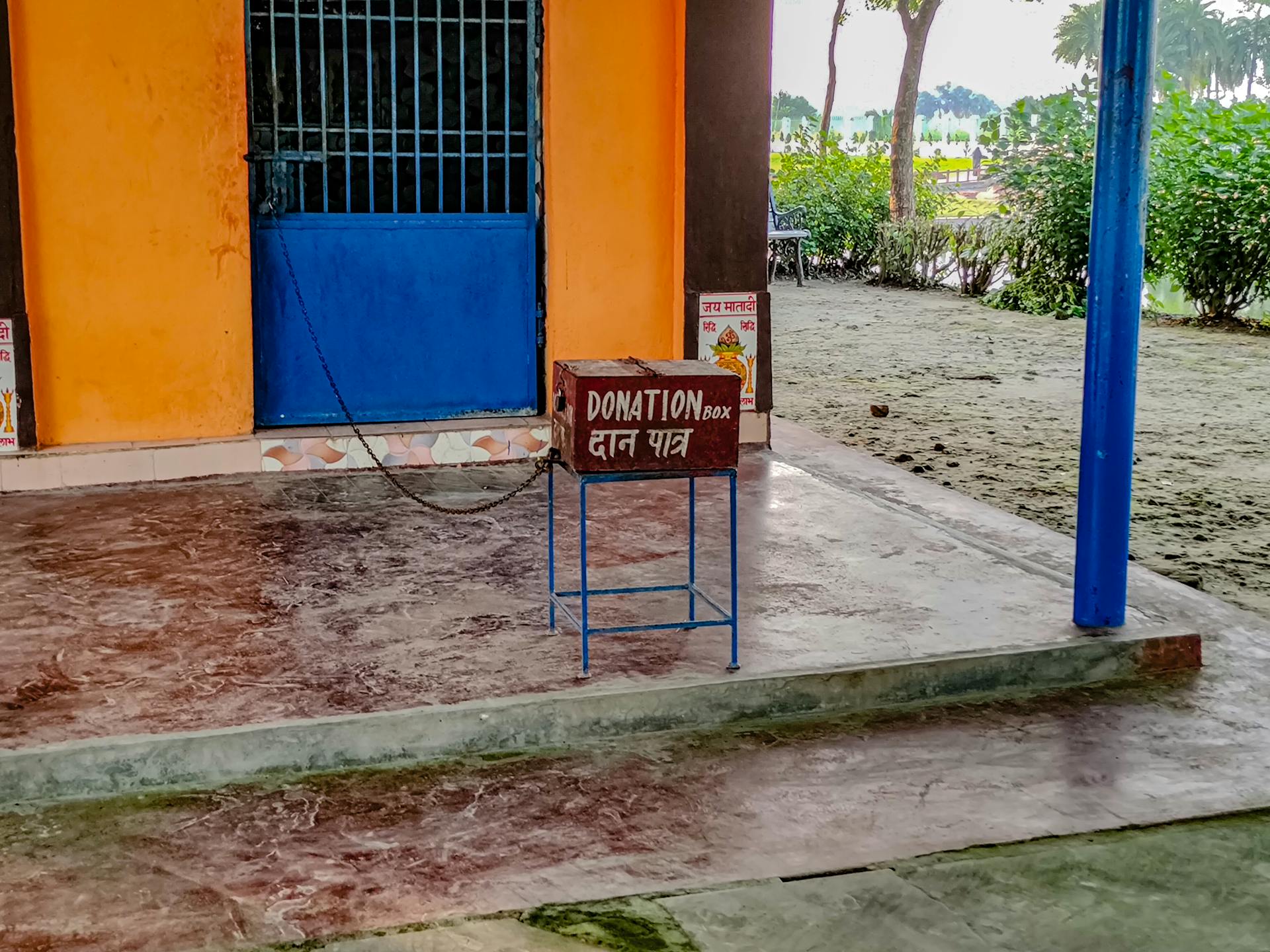 A donation box placed in front of a vibrant orange and blue building entryway in India.