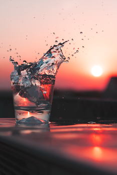 Dramatic splash of water in a glass against a vibrant sunset backdrop. Perfect for refreshment themes.