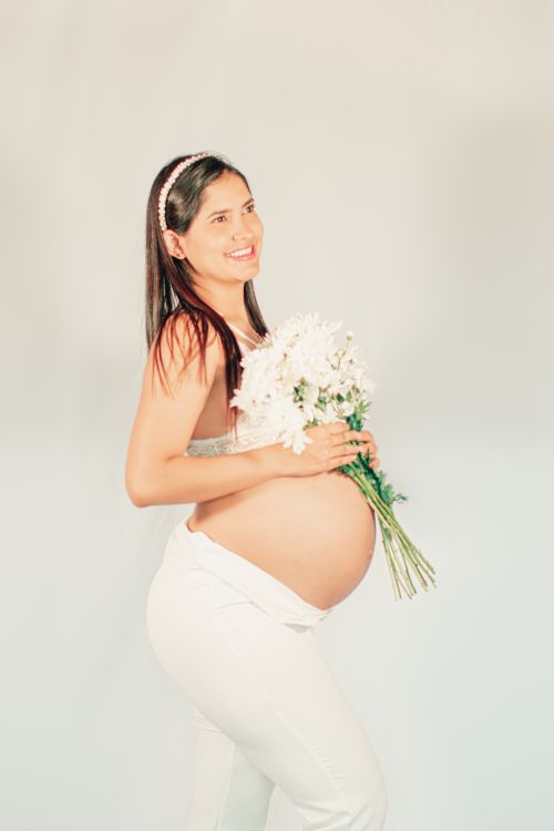 Free Smiling pregnant woman holding flowers in a studio setting, exuding joy and warmth. Stock Photo