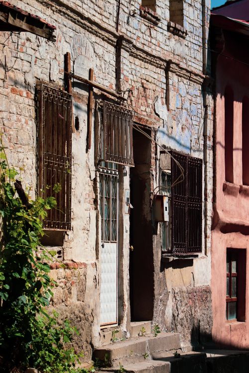 Free A weathered brick facade with a gated entrance and overgrown plants, capturing urban decay. Stock Photo