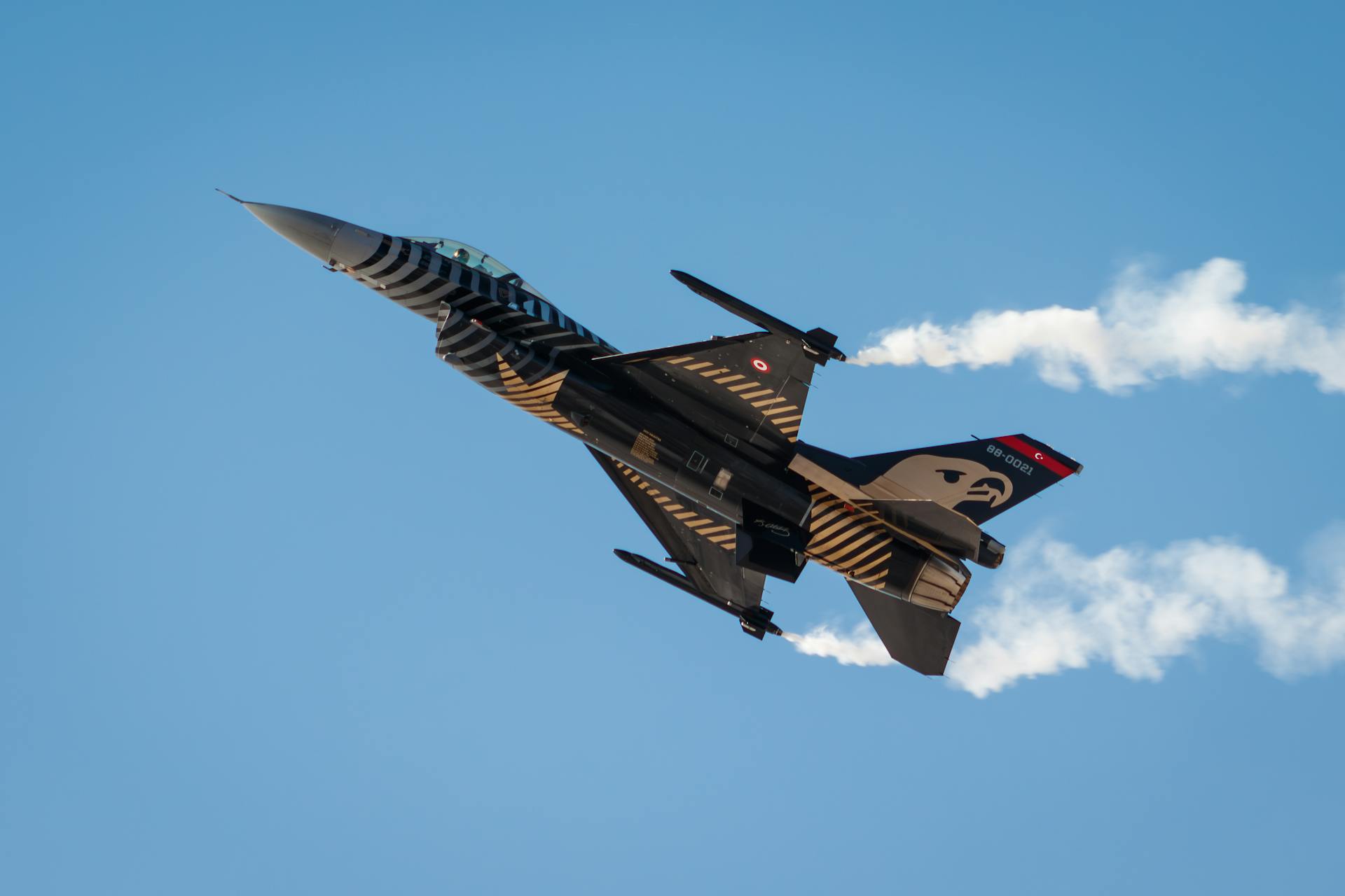 Military jet with tiger stripes performing aerobatics against a clear blue sky.