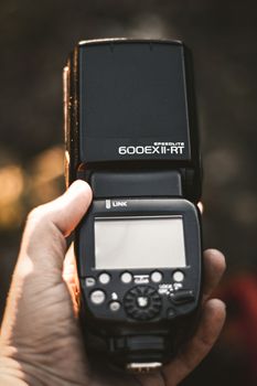 Vertical shot of a speedlite flash held outdoors, capturing advanced photography equipment.