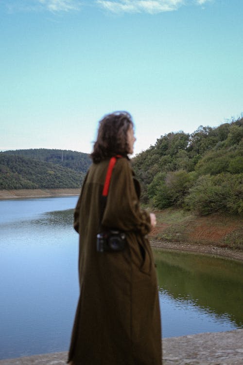 A woman in a long coat standing near a lake