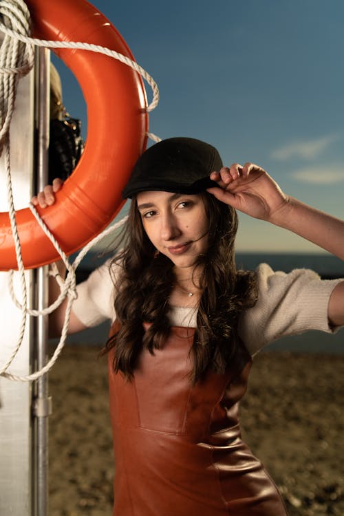 A woman in a leather dress and hat posing near a life preserver
