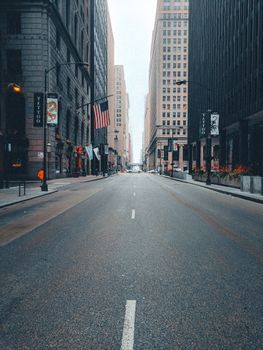 A deserted city street flanked by tall buildings and USA flags, capturing urban architecture.