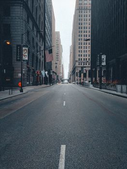 A peaceful, empty city street lined with skyscrapers, featuring American flags and tattoo signs.