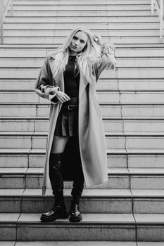 Stylish woman in a trench coat poses on stairs in a modern urban setting.