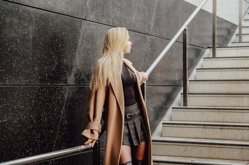 Blonde Woman in Coat Standing by Wall on Stairs