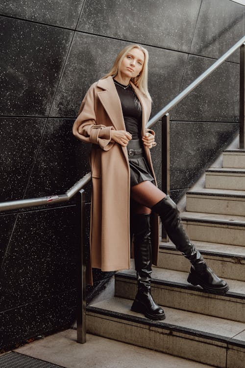 Woman in a Coat and Boots Posing on a Staircase